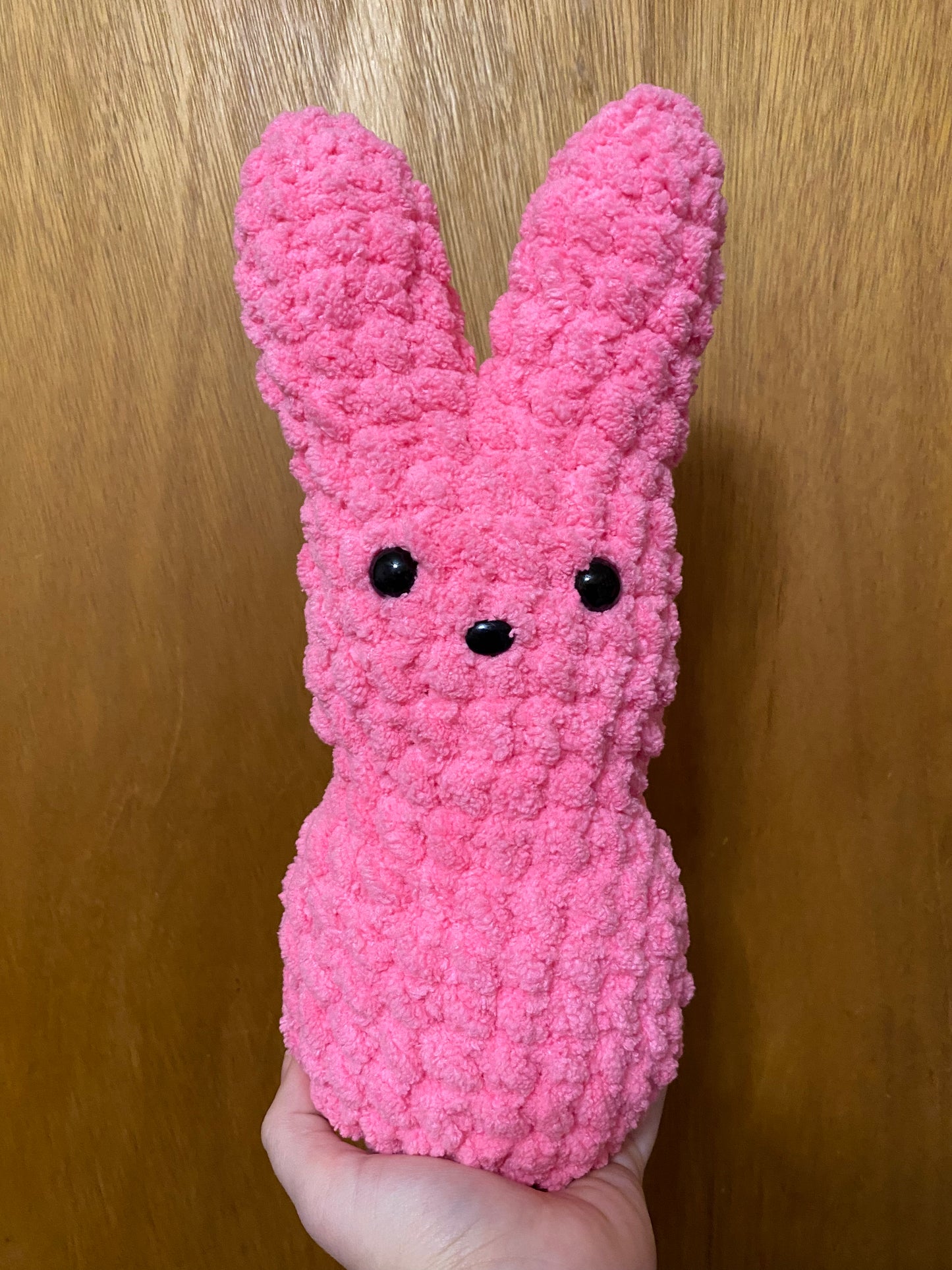 Pink textured bunny toy held against a wooden background